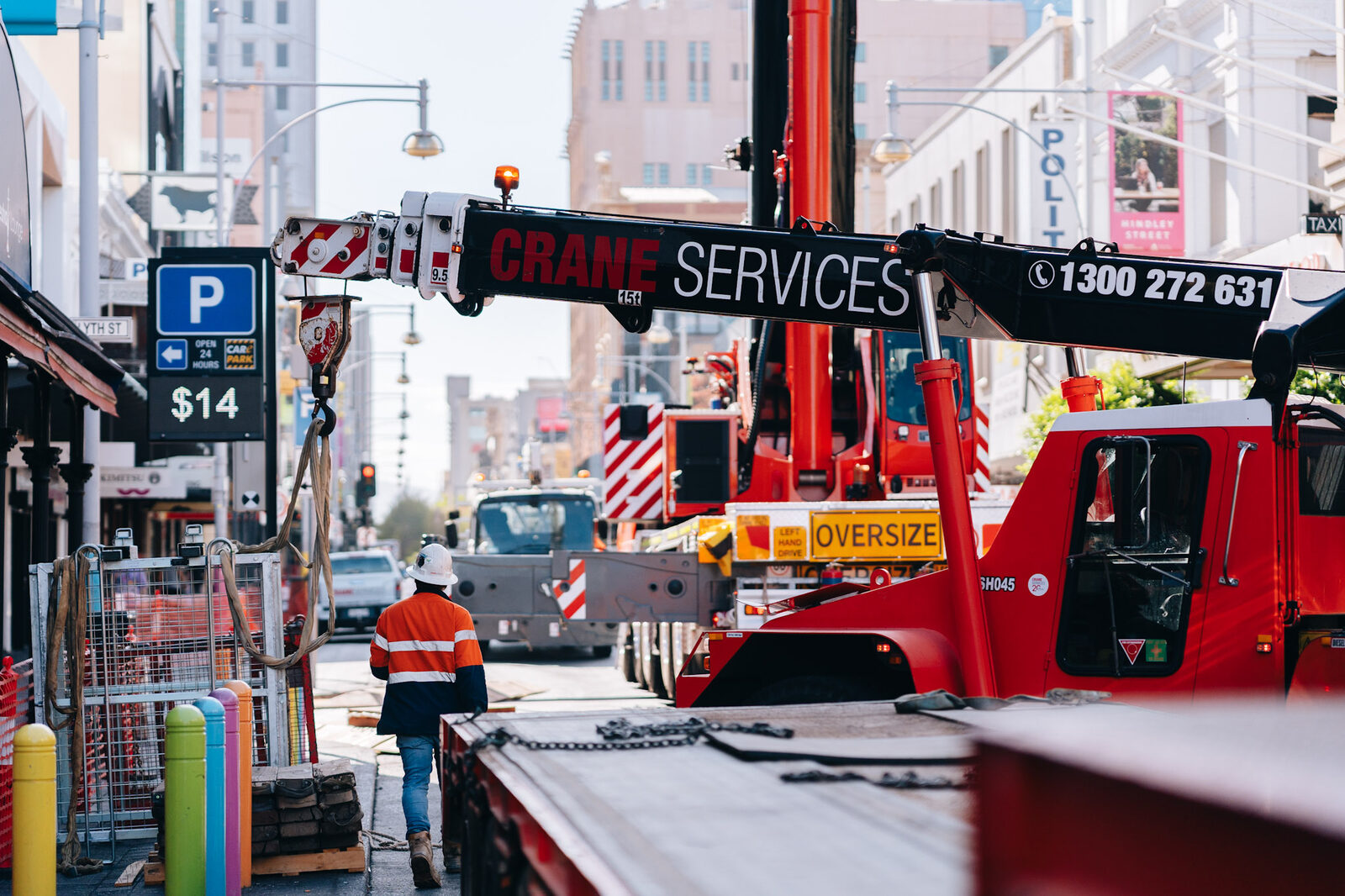 The front of a mobile crane with its outriggers set on pads across a city street, oversize sign on the bumper.